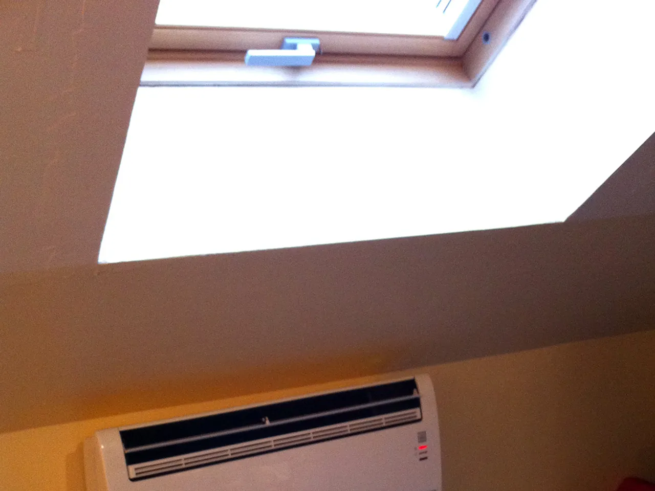 Console de climatisation murale posee sous un velux dans une chambre amenagee en combles