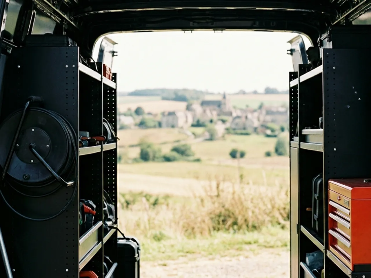 Vue depuis l'interieur d'un utilitaire de service, portes ouvertes sur un paysage rural, materiel bien range